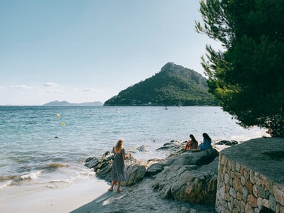 Three women sit on the rocks of the seaside
